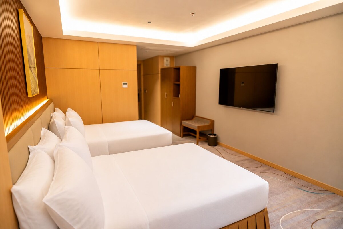 Ein Hotelzimmer mit zwei Betten, einem Fernseher, einem Schreibtisch und einem Kleiderschrank.