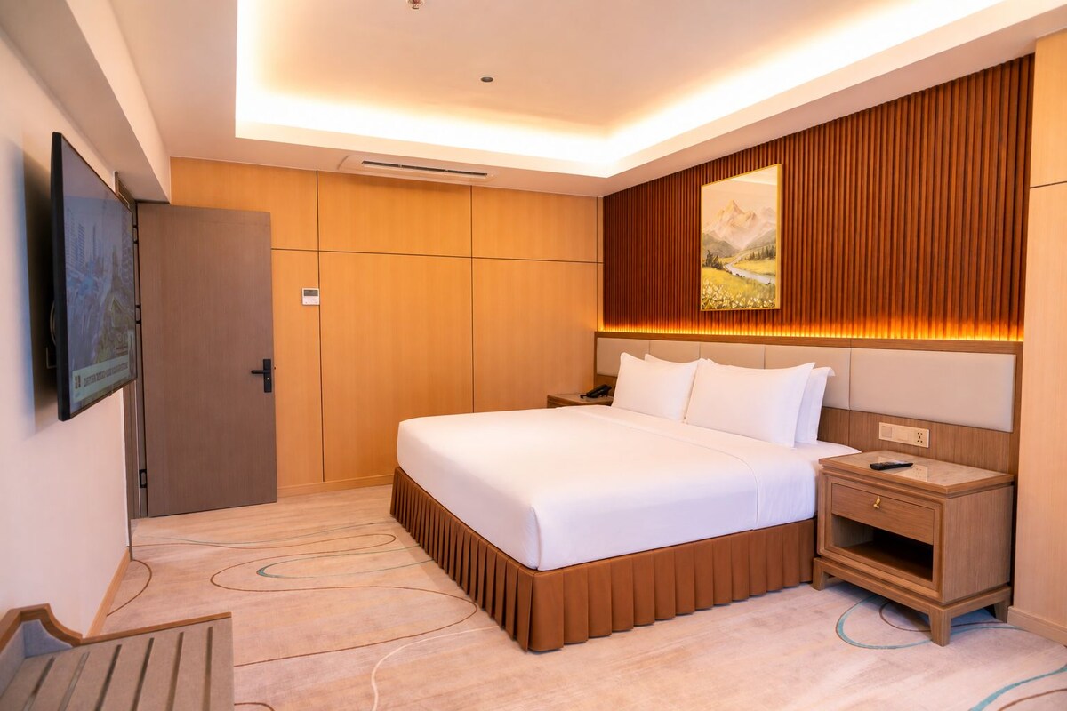 Ein Hotelzimmer mit einem großen Bett, Nachttisch und einem an der Wand montierten Fernseher.