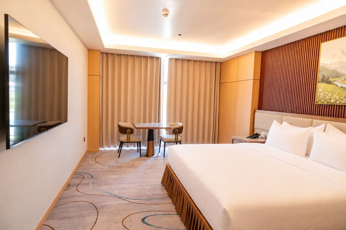 Ein Hotelzimmer mit einem großen Bett, einem Schreibtisch mit zwei Stühlen, einem Fernseher und einem Gemälde an der Wand.
