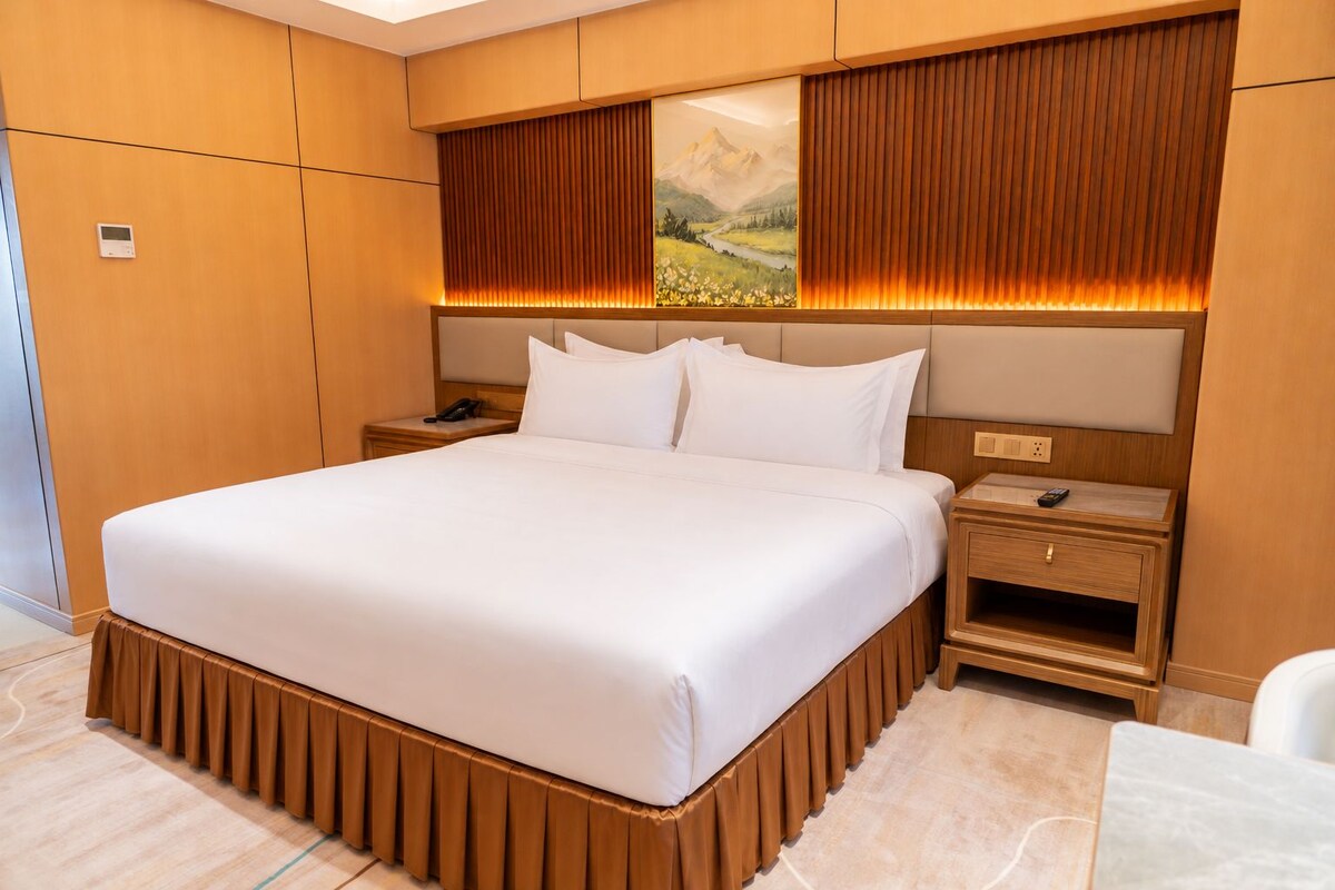Ein modernes Hotelzimmer mit einem großen Bett, einem Holzkopfteil, Nachttischen und einem Landschaftsbild.