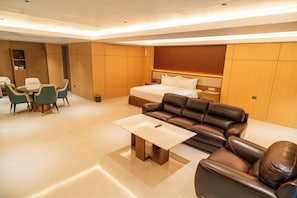 A modern hotel room with a large bed, a leather sofa, a dining table with chairs, and a small kitchen area. - The One Hotel (Piura)