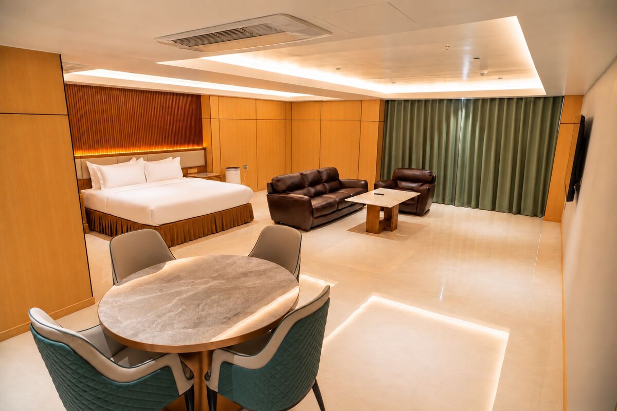 Ein modernes Hotelzimmer mit einem Bett, einer Couch, einem Esstisch und einem Fernseher.