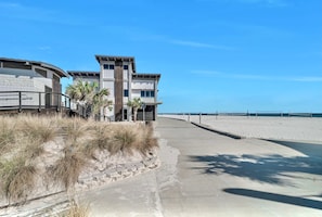 En ejendom ved stranden med en buet bygning, en sti af beton og en sandstrand.