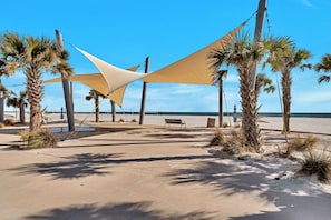 En strandpromenade med palmer, en bænk og en stor parasol.