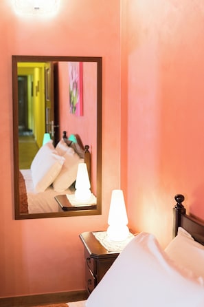 Ein Hotelzimmer mit Bett, Nachttisch, Lampe und einem Spiegel, der den Raum widerspiegelt.
