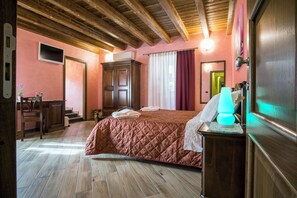 Ein Schlafzimmer mit Holzboden, einem Bett mit roter Steppdecke, einem Nachttisch mit Lampe und einem Holzschrank.