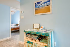 Een kamer met een bed, een aan de muur bevestigd schilderij en een tafeltje met boeken en een bord.