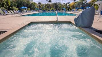 A swimming pool with a water fountain feature, surrounded by lounge chairs and umbrellas.