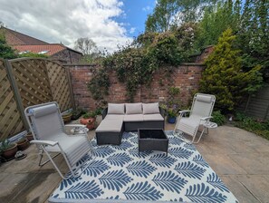 Une terrasse avec un canapé, deux fauteuils et un tapis à motifs.