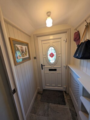 A white door with a glass panel and a red flower design, a framed picture on the wall, and a black bag hanging on a hook. - Charming Yorkshire Cottage | Log Burner | Dog Friendly | Near Malton (Brawby)