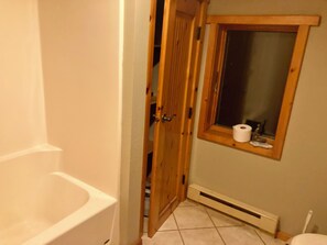 Een badkamer met een badkuip, toilet en een raam met houten kader.