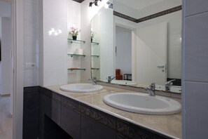 Une salle de bain avec deux lavabos, un grand miroir et une étagère en verre où sont rangés les articles de toilette.