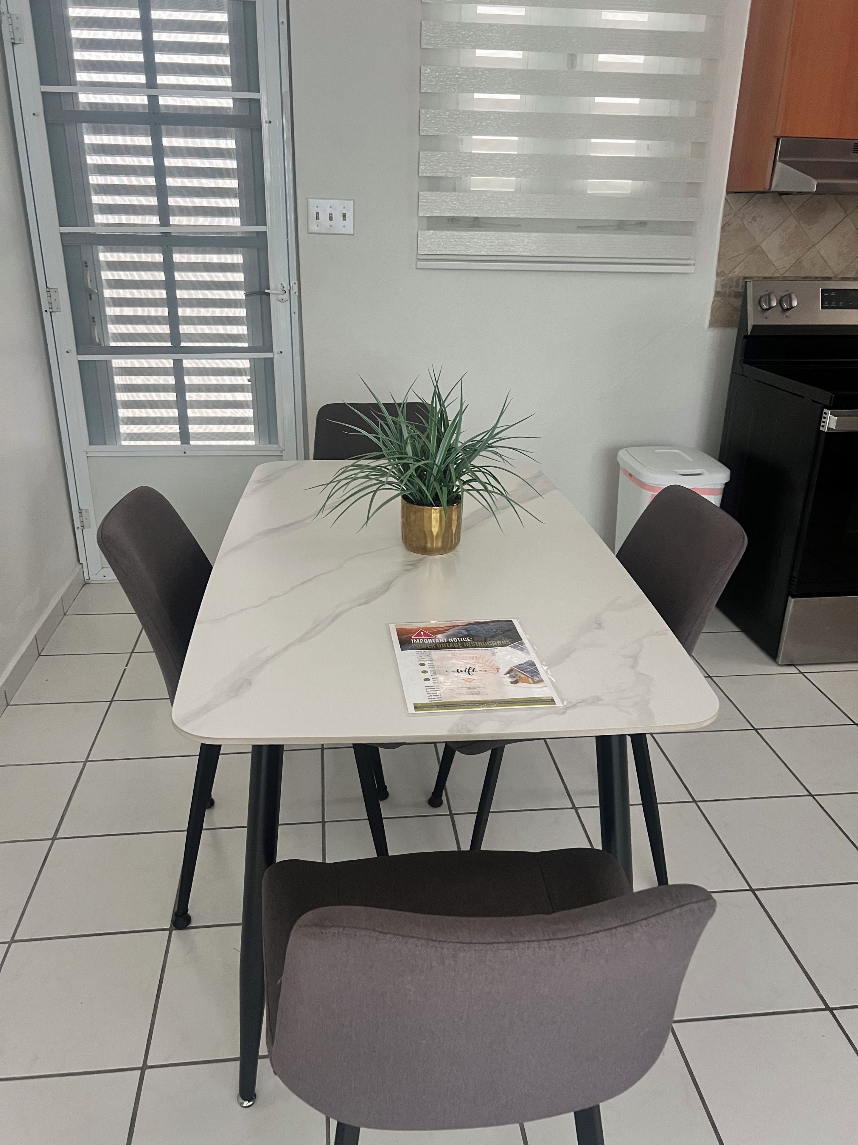Un coin repas avec une table en marbre blanc, quatre chaises, une plante en pot et une affiche posée sur la table.