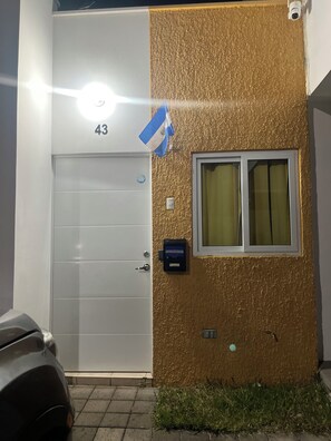 Ein Gebäude mit einer weißen Tür, die mit der Nummer 43 gekennzeichnet ist, einem Fenster mit Vorhängen und einer Überwachungskamera.