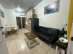 Una sala moderna con un sofá negro, una mesa de centro de madera y un comedor con una mesa y sillas blancas.