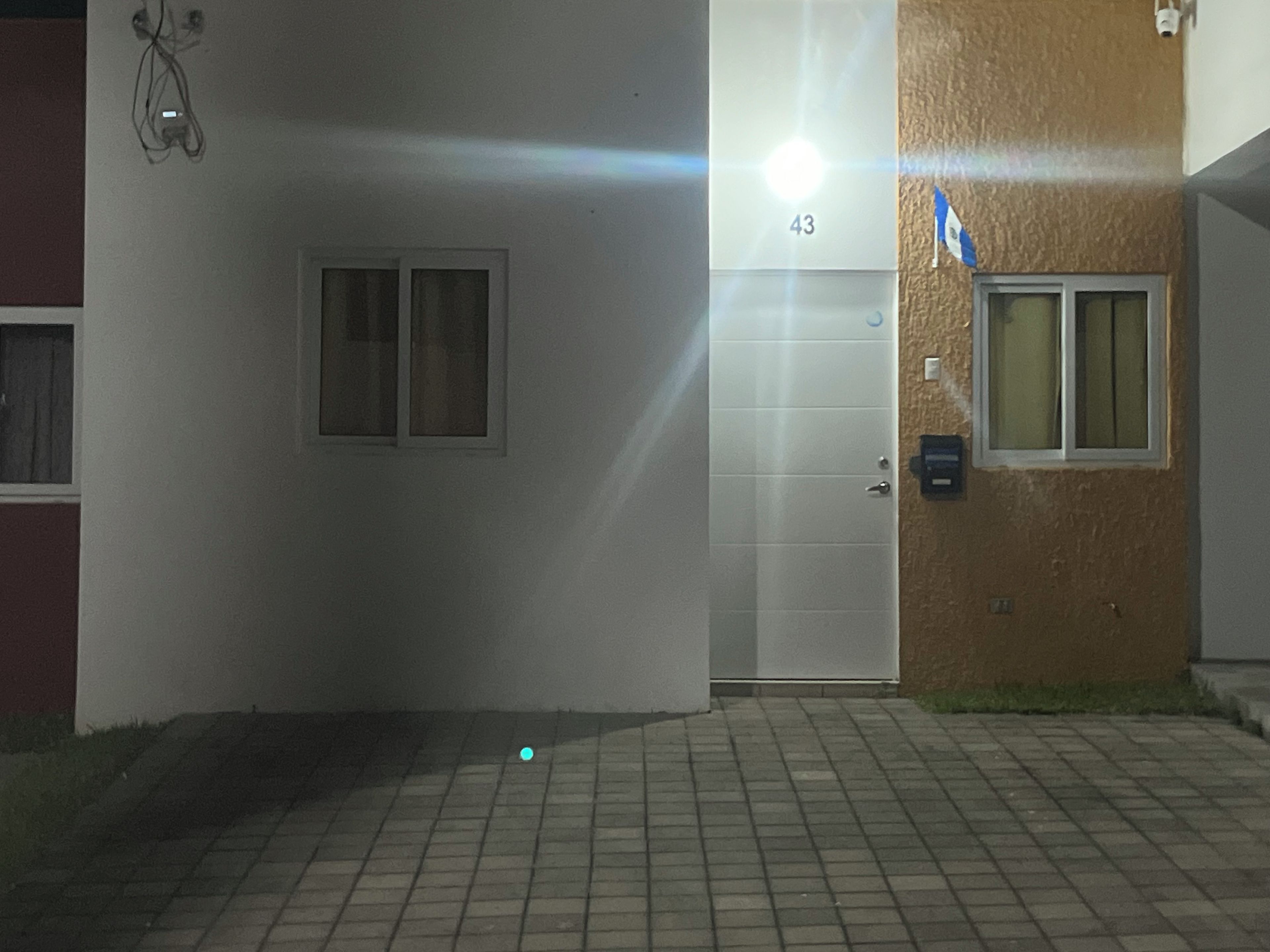 En byggnadsentré med en vit dörr som är märkt med nummer 43, ett litet fönster och en övervakningskamera på väggen.