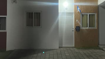 En byggnadsentré med en vit dörr som är märkt med nummer 43, ett litet fönster och en övervakningskamera på väggen.