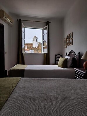 Een hotelkamer met een bed, een raam met gordijnen, een nachtkastje en een wandlamp.