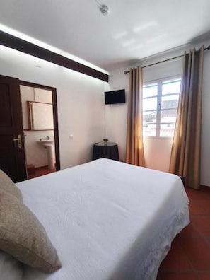 Een hotelkamer met een bed, een flatscreen televisie aan de muur, een raam met gordijnen en een deur naar een andere kamer.