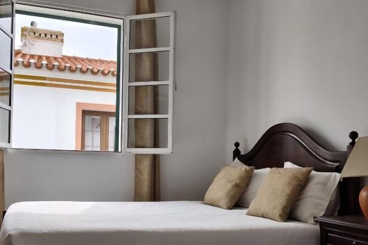 Een kamer met twee bedden, een raam met gordijnen en uitzicht op een gebouw.