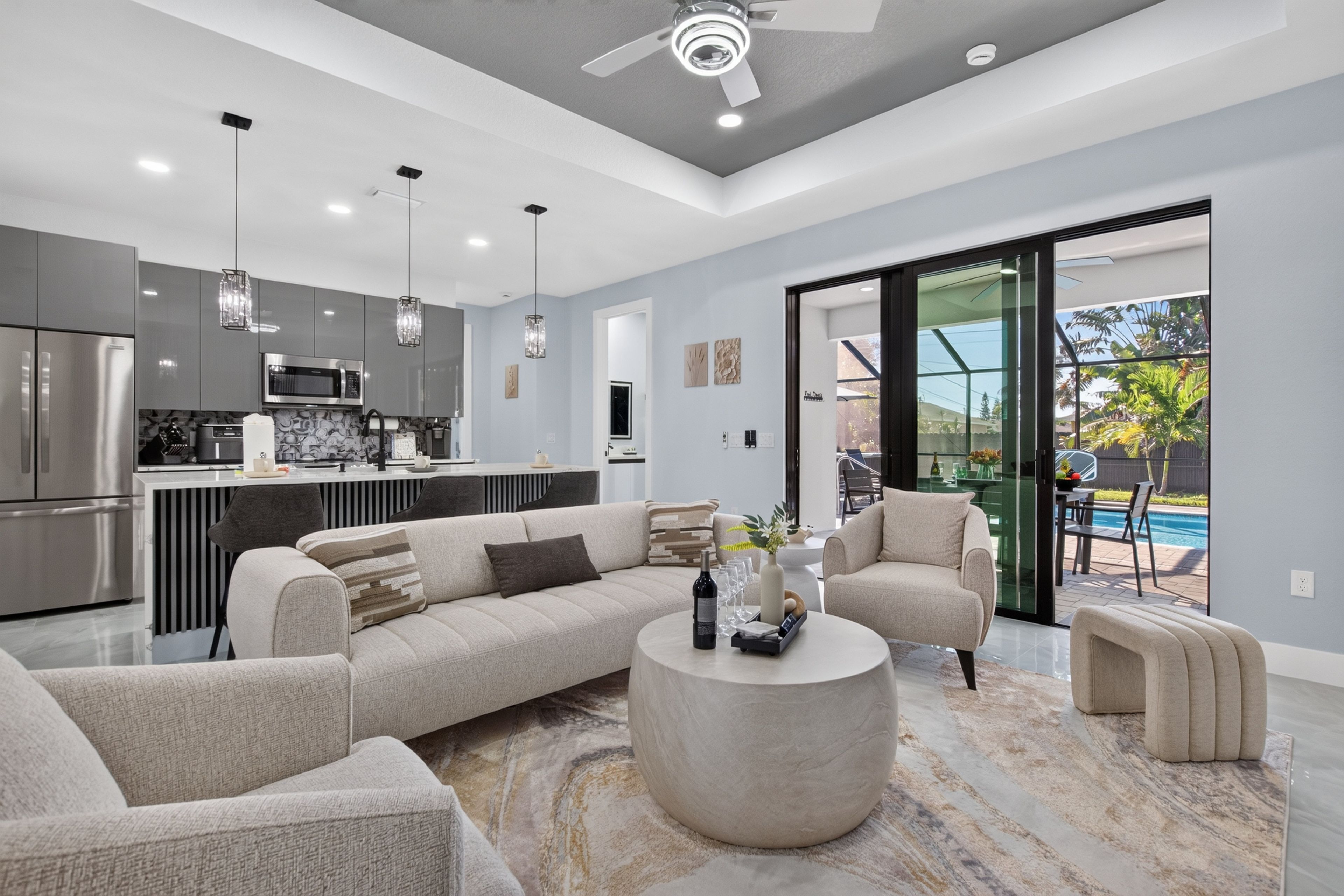 A modern kitchen with stainless steel appliances, a dining area with a sofa and chairs, and a view of a pool through a glass door.