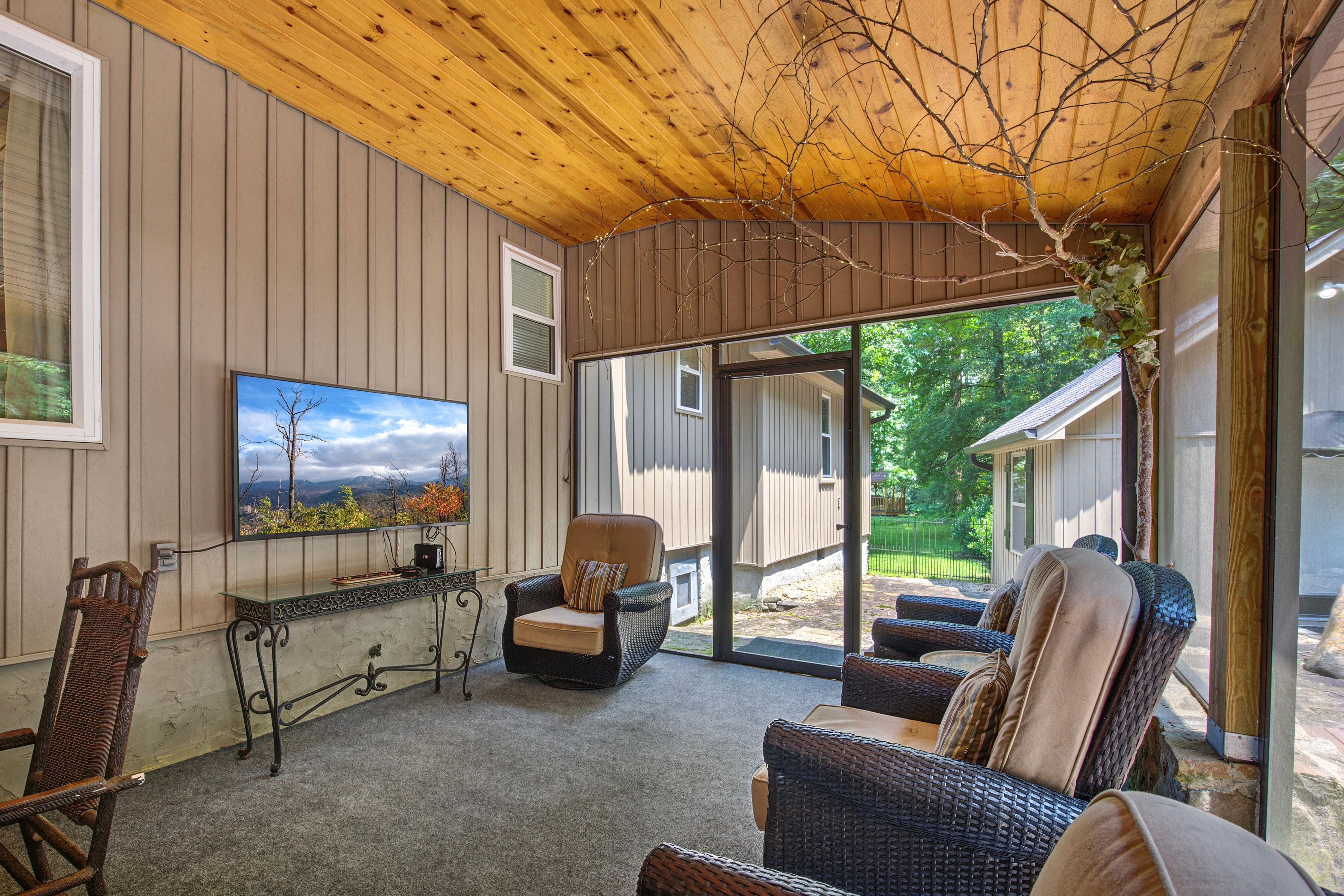 A covered patio area with wicker furniture, a television, and a view of the outdoors.