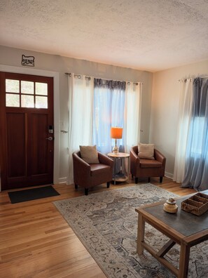 A living room with a wooden door, two leather armchairs, a small round table with a lamp, a patterned rug, and a wooden coffee table. - The Blackberry Cottage 2-bedroom house in beautiful Bend for relaxing stays! (Bend)