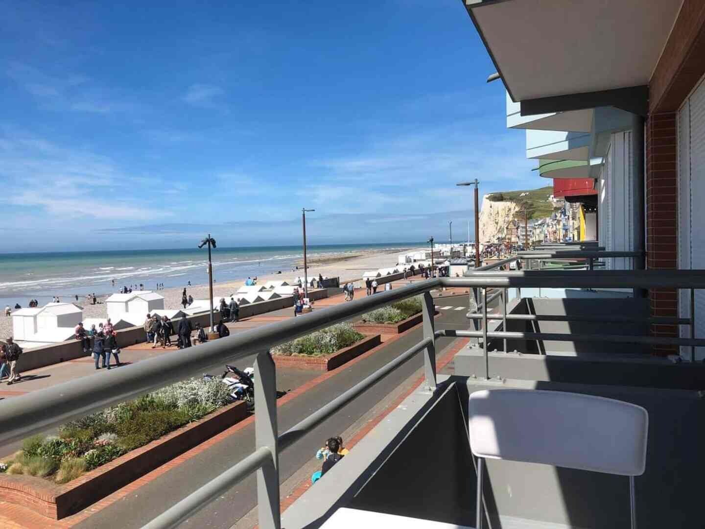 A balcony with a view of a beach and promenade, featuring a railing and a chair.