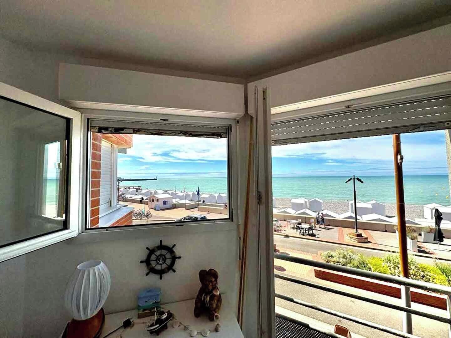 Ett rum med ett stort fönster med utsikt över en strand, en modell av ett skepp och en nallebjörn.