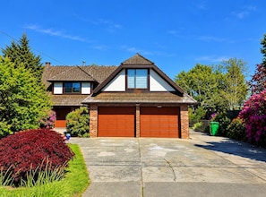 A two-story house with a garage, surrounded by well-maintained gardens and trees. - Vancouver Airport Tudor House - 2000sf (Richmond)