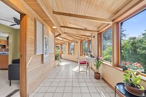 A covered patio area with a tiled floor, wooden ceiling beams, and large windows offering a view of the outdoors. - Vancouver Airport Tudor House - 2000sf (Richmond)