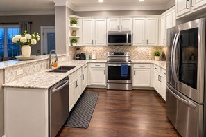 A modern kitchen with white cabinets, stainless steel appliances, a herringbone tile backsplash, and a wooden floor. - Luxury Getaway Near Lake Lanier / Sleeps 10 (Buford)