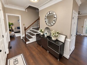 A spacious hallway with a wooden staircase, a dark-toned console table with decorative items, and a mirror on the wall. - Luxury Getaway Near Lake Lanier / Sleeps 10 (Buford)