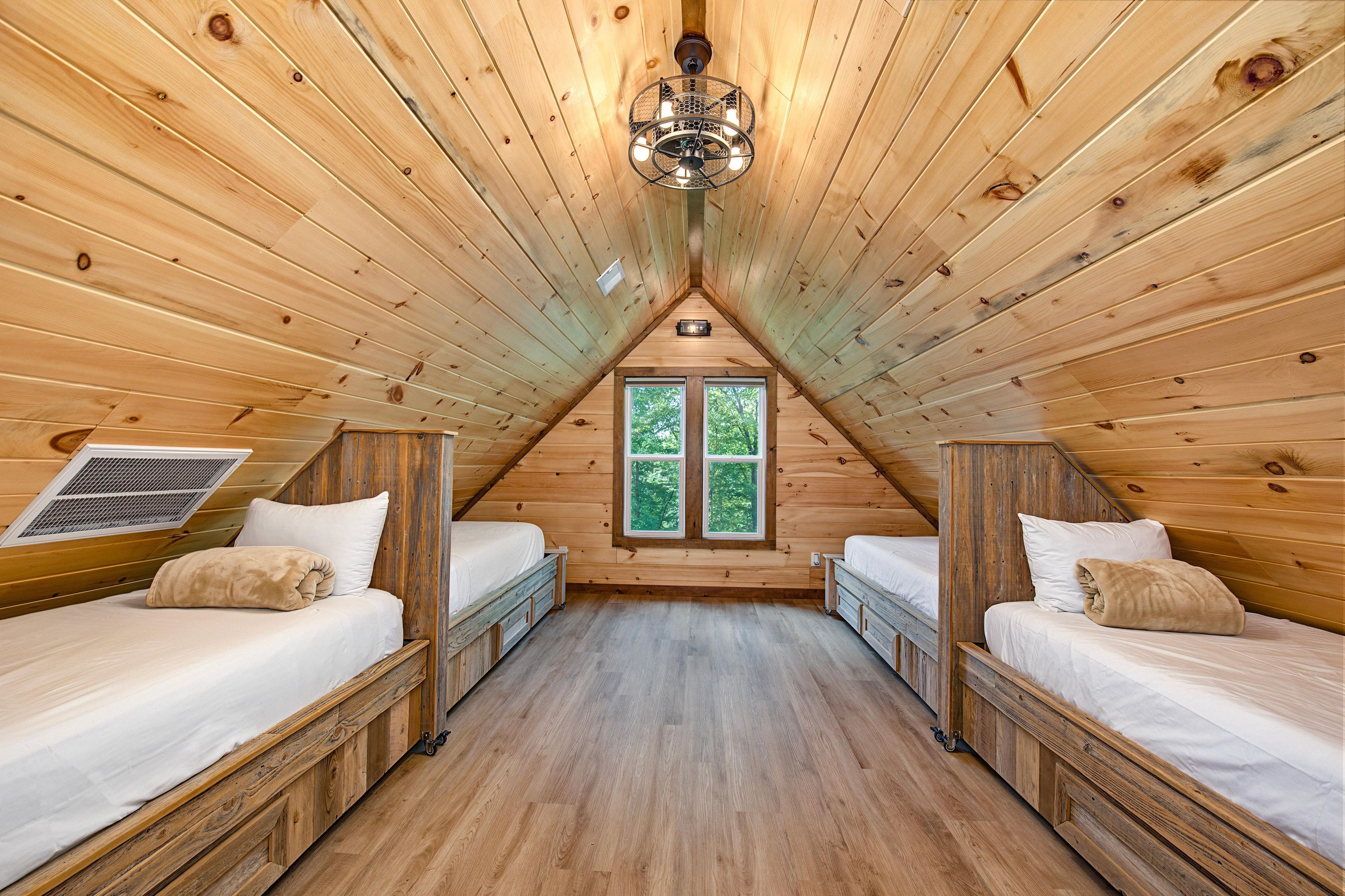 Une cabane en bois avec deux lits superposés, un plafond en pente et une fenêtre donnant sur les arbres.