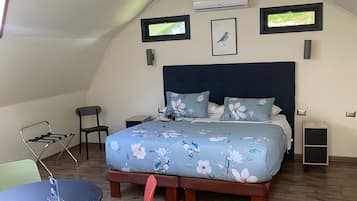 Un dormitorio con una cama grande, una mesita, dos sillas y un tragaluz.