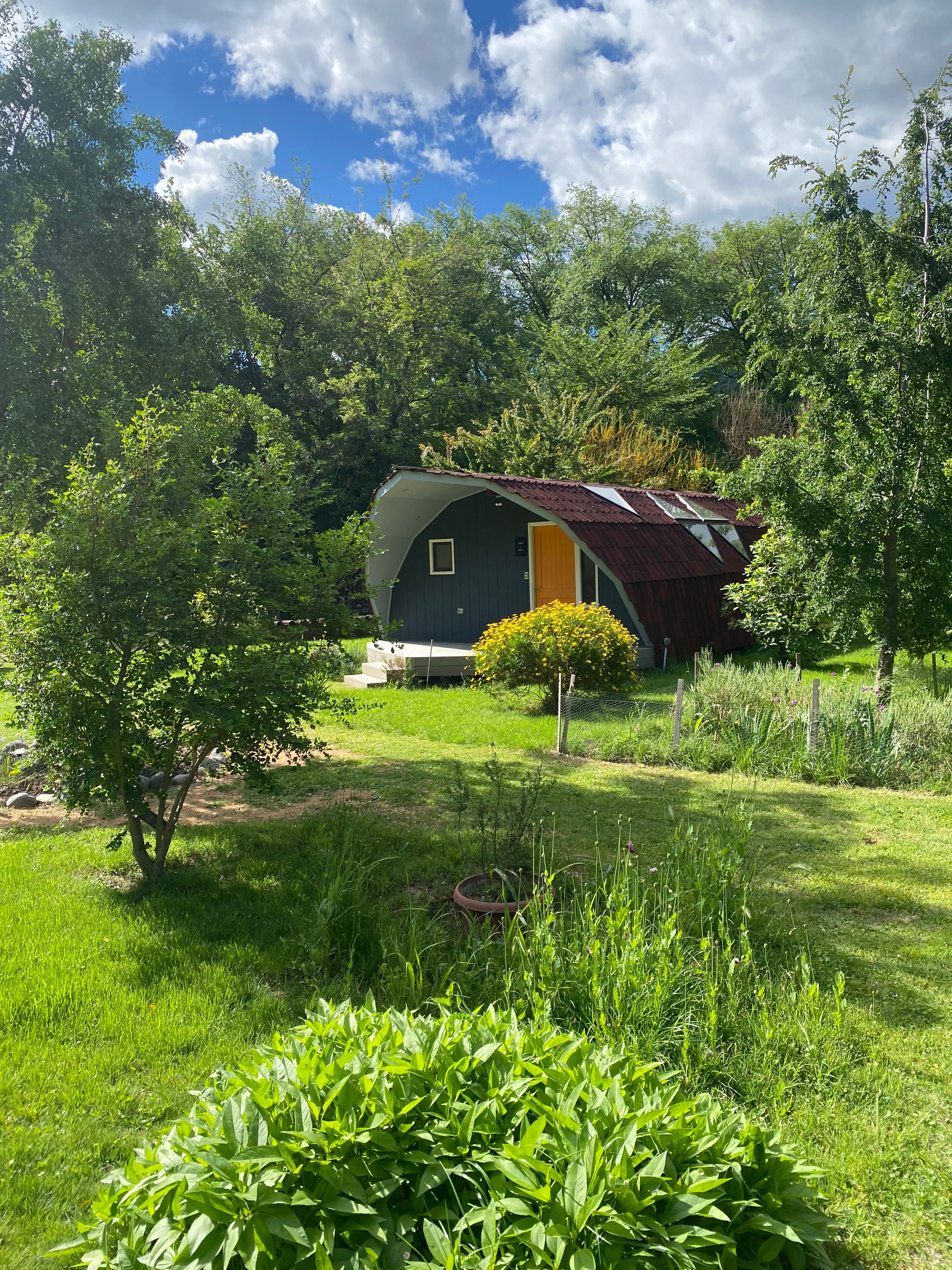 A rustic cabin with a sloped roof, surrounded by lush greenery and trees.