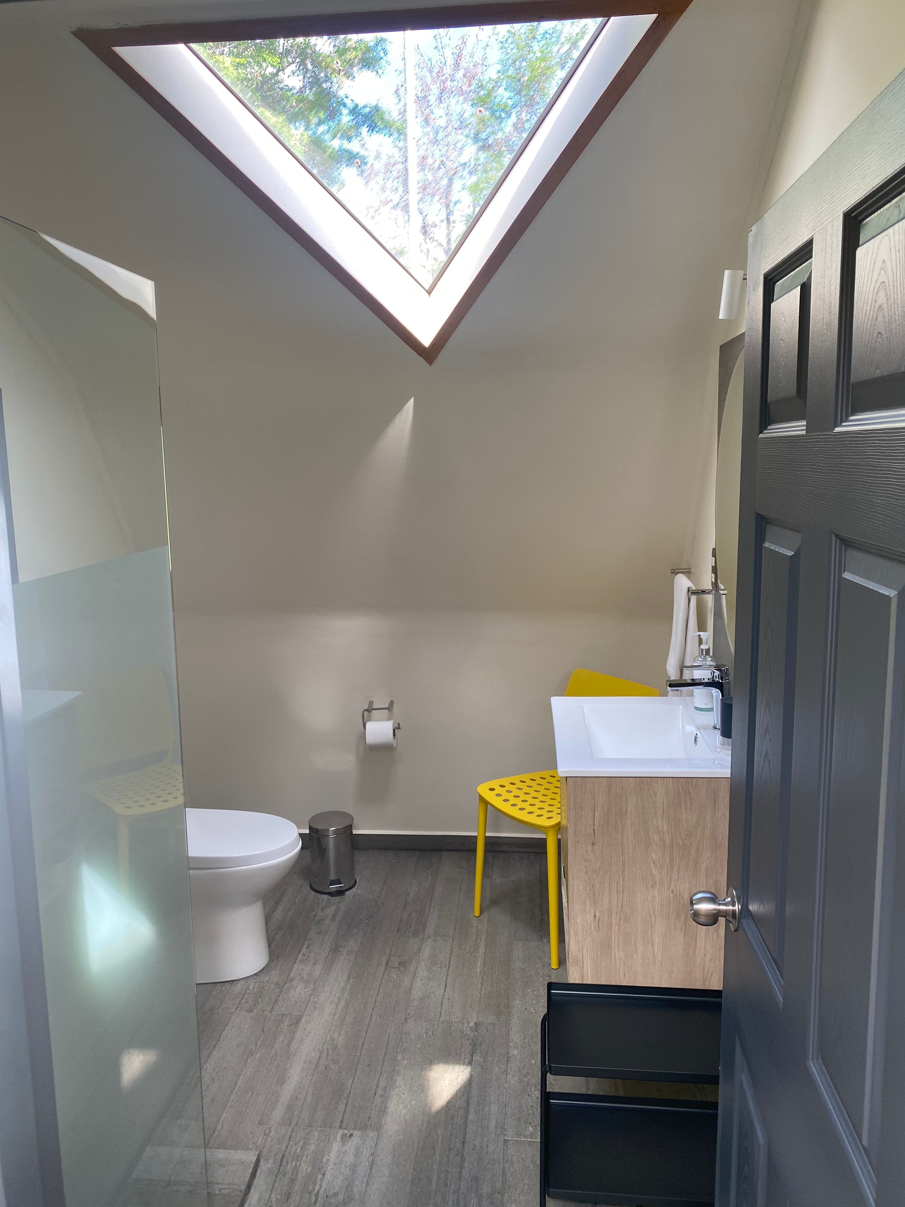 Un baño pequeño con tragaluz, inodoro, lavamanos y una silla amarilla.