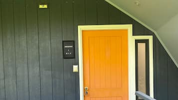 Una puerta de madera oscura con un panel naranja brillante, un buzón y una ventana pequeña.