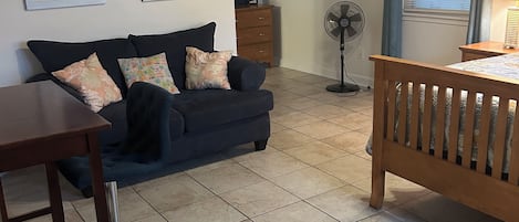 Una sala de estar con un sofá, una mesa de madera, un ventilador y una ventana con persianas.