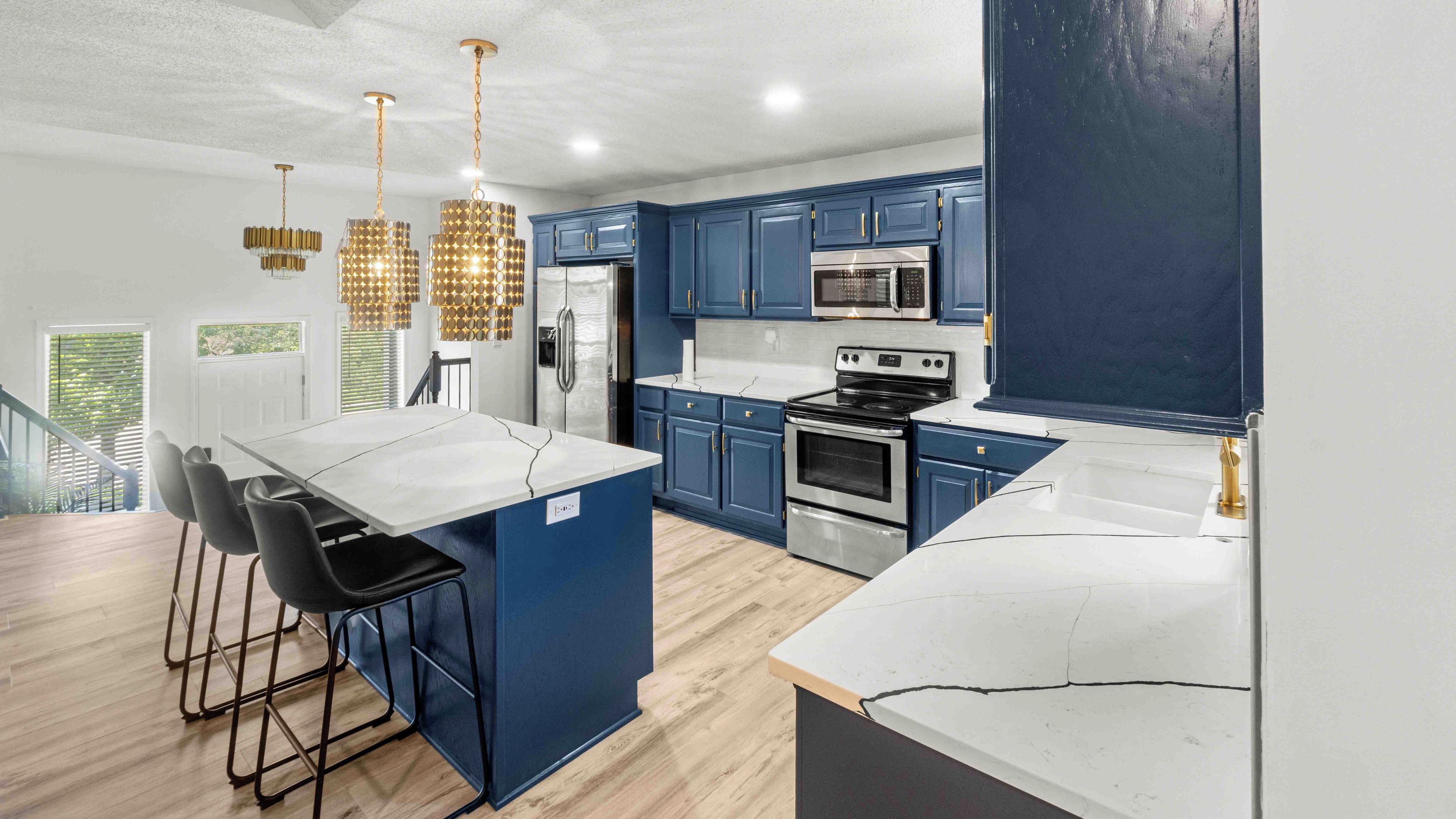 Une cuisine moderne avec des meubles bleus, un îlot central blanc, des appareils en acier inoxydable et des luminaires suspendus.