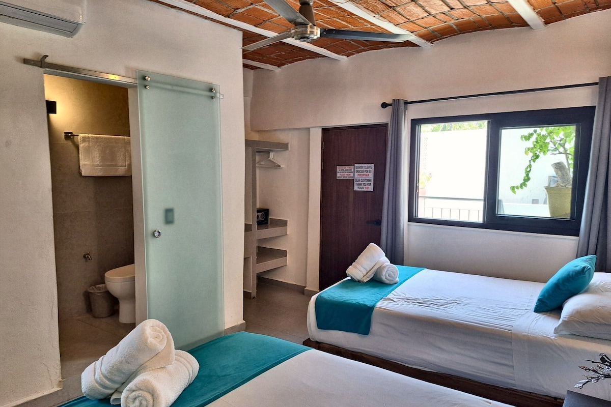 Habitación de hotel con dos camas, baño y ventana con vistas.
