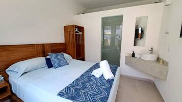 Habitació d'hotel amb un llit, un armari de fusta, un bany amb un rentapeus i un mirall, i una vista a través d'una porta de vidre.