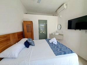 A hotel room with a bed, a wooden wardrobe, a bathroom with a sink and mirror, and a TV mounted on the wall. - Amani Bucerias (Bucerías)