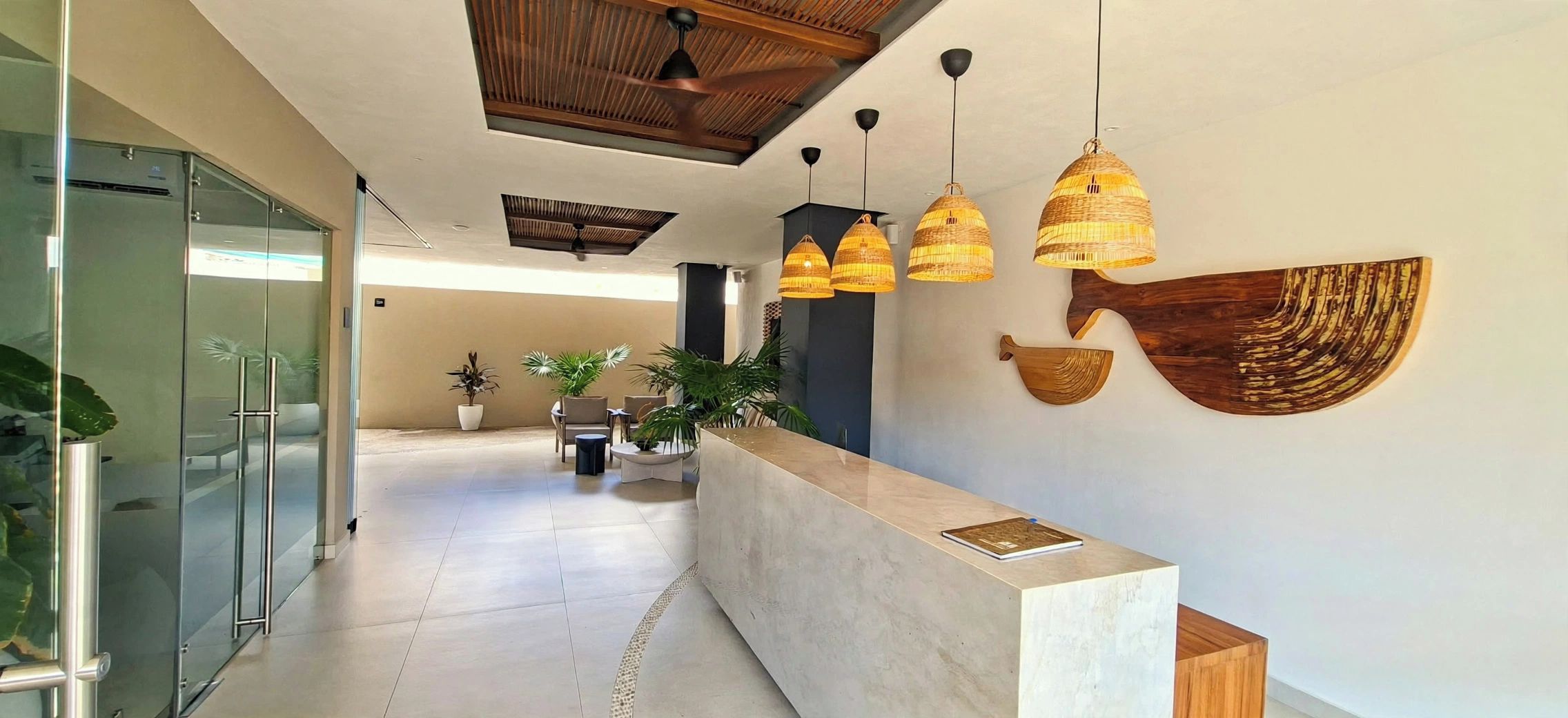 Un espace d’accueil moderne avec un comptoir en marbre, des lampes suspendues en osier et un grand élément décoratif fixé au mur.