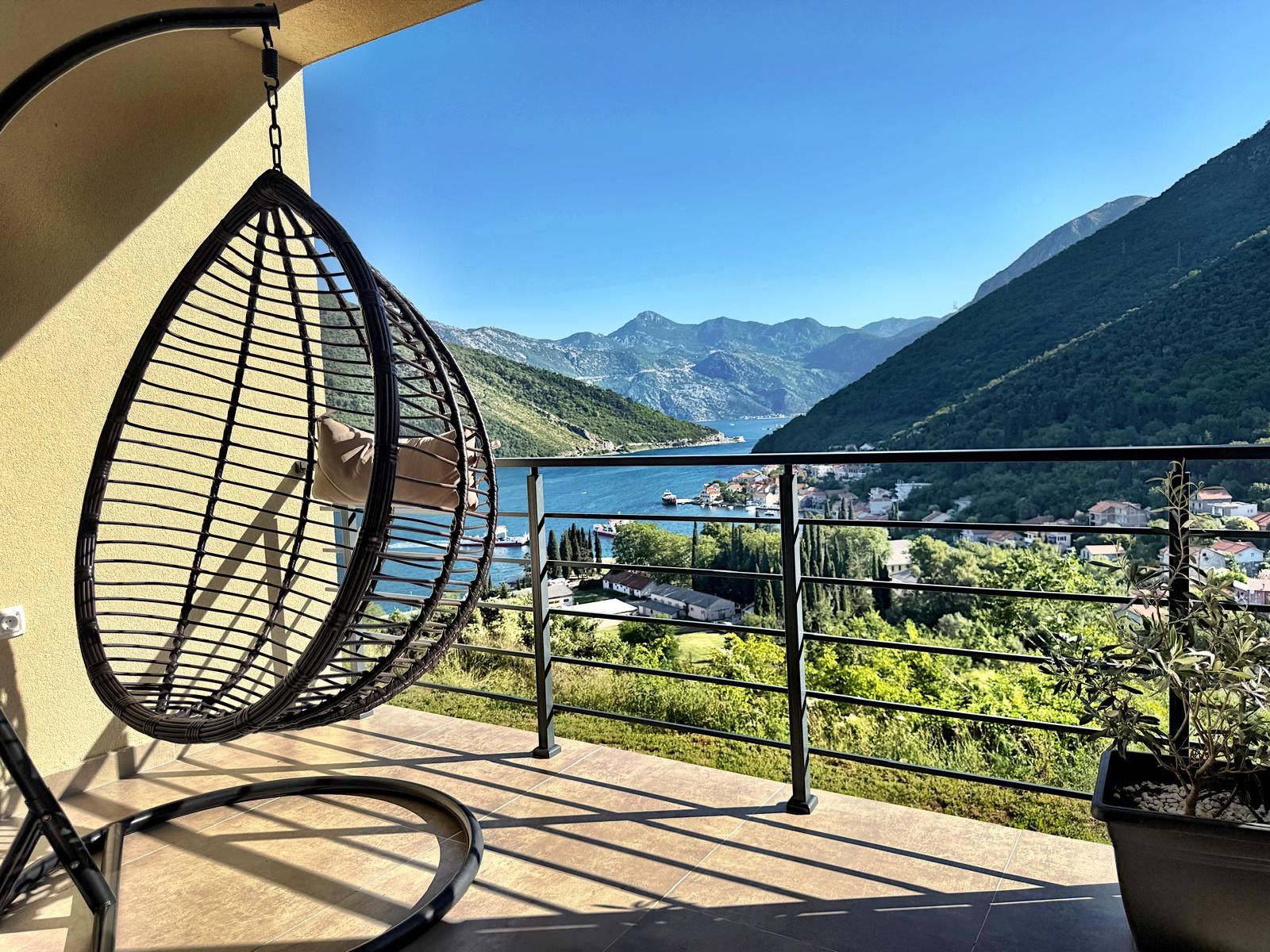 Ein Balkon mit einer Hängematte, einem Blumentopf und Blick auf einen See und Berge.