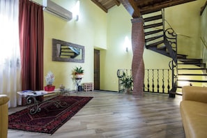 Ein geräumiger Wohnbereich mit Holzboden, einem roten Vorhang, einer Treppe und einem Sofa.