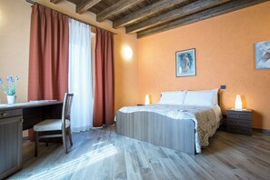 Ein Schlafzimmer mit Bett, Nachttisch, Lampe, Schreibtisch, Stuhl und Vorhängen.