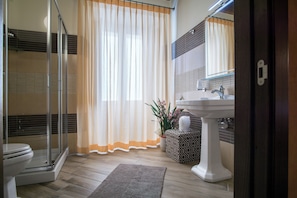Ein Badezimmer mit Glasdusche, Toilette, Waschbecken mit Spiegel und einer Topfpflanze.