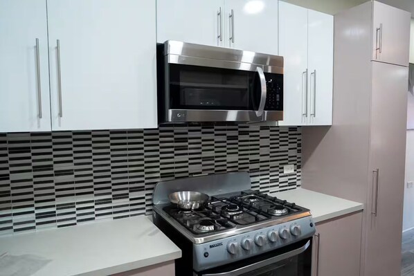 A kitchen with white cabinets, a stainless steel microwave, and a gas stove. - Gulf Residence Apt2 (La Romain)