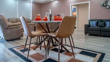 A dining area with a glass table, four chairs, and a patterned rug.